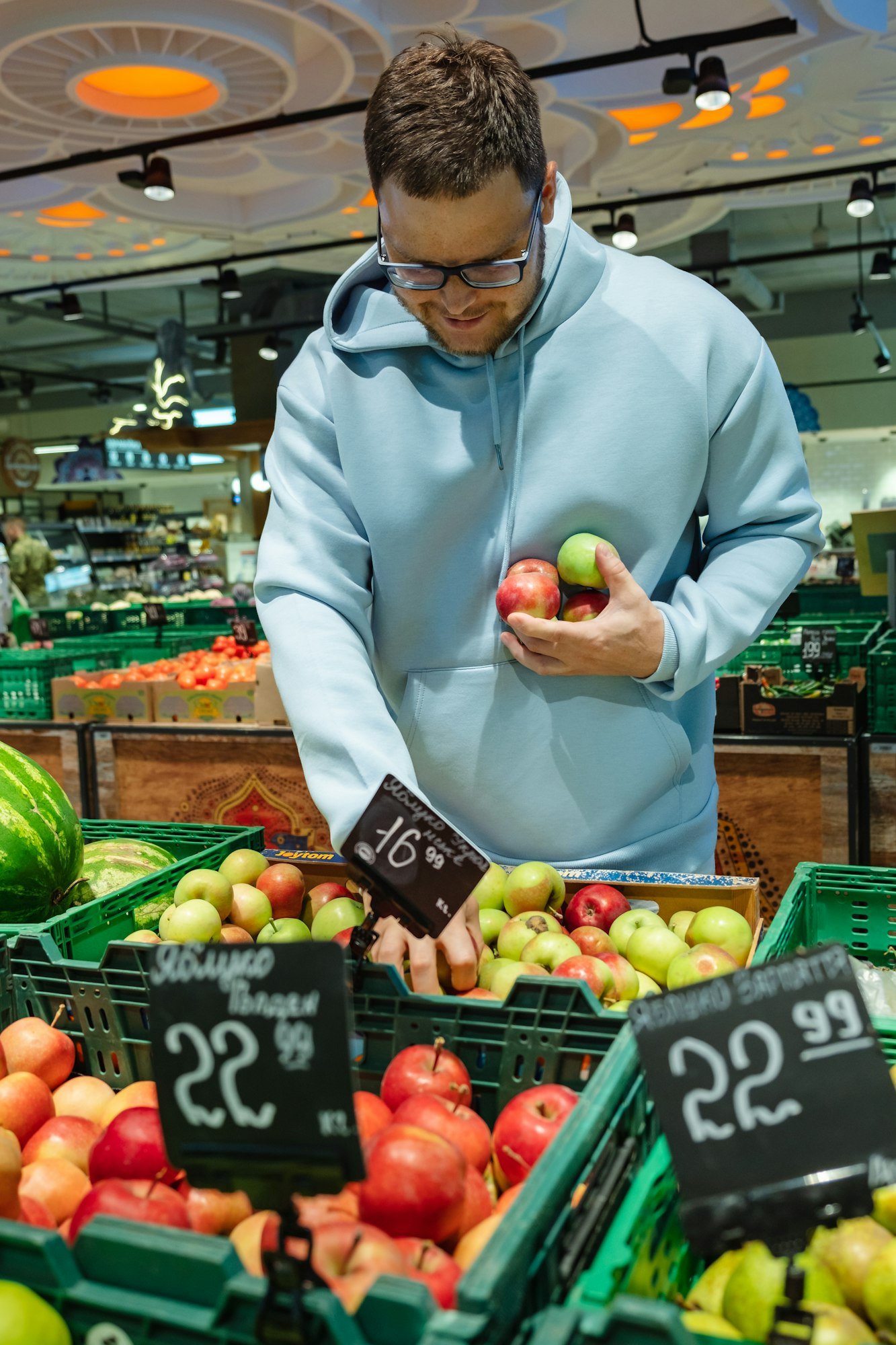 A man buys food, . A male customer chooses apples, taking products from the shelves